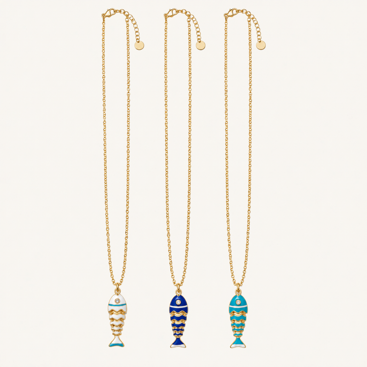 Three gold chain necklaces with fish-shaped pendants, displayed vertically on a light cream background. The left and right necklaces feature light blue and white patterned fish, while the center necklace features a dark blue and yellow striped fish.
