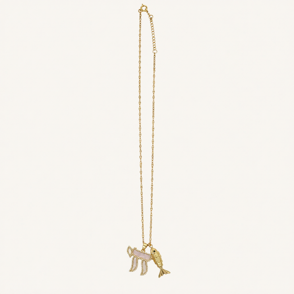 A gold chain necklace featuring a pendant with a pink and white striped flag and a gold fish, displayed against a solid off-white background.