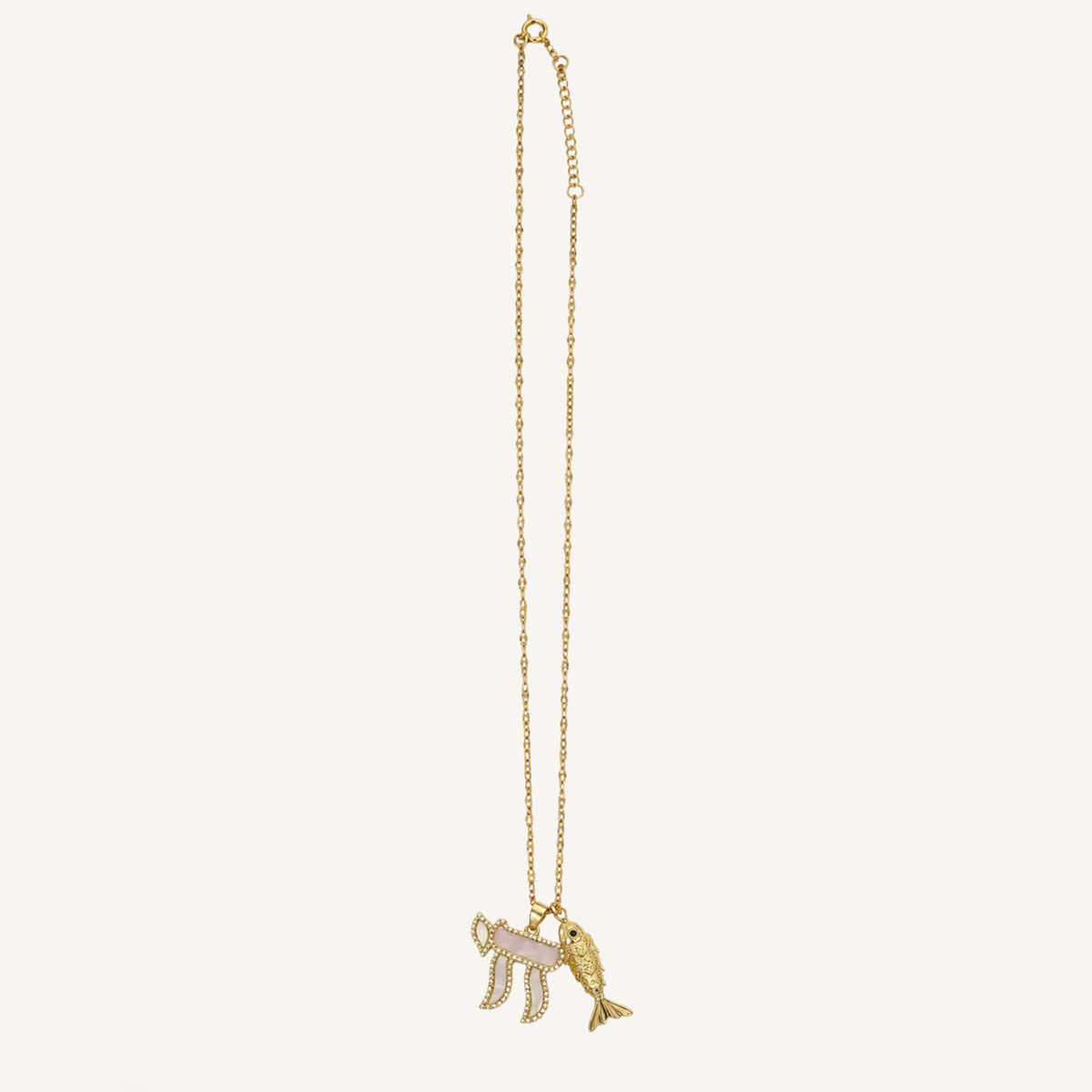 A gold chain necklace featuring a pendant with a pink and white striped flag and a gold fish, displayed against a solid off-white background.