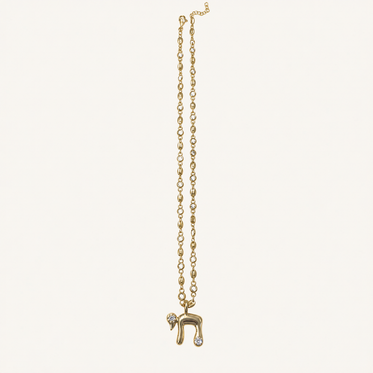 A delicate gold chain necklace featuring a Hebrew letter 'Heh' pendant adorned with small clear stones, displayed against a solid off-white background.