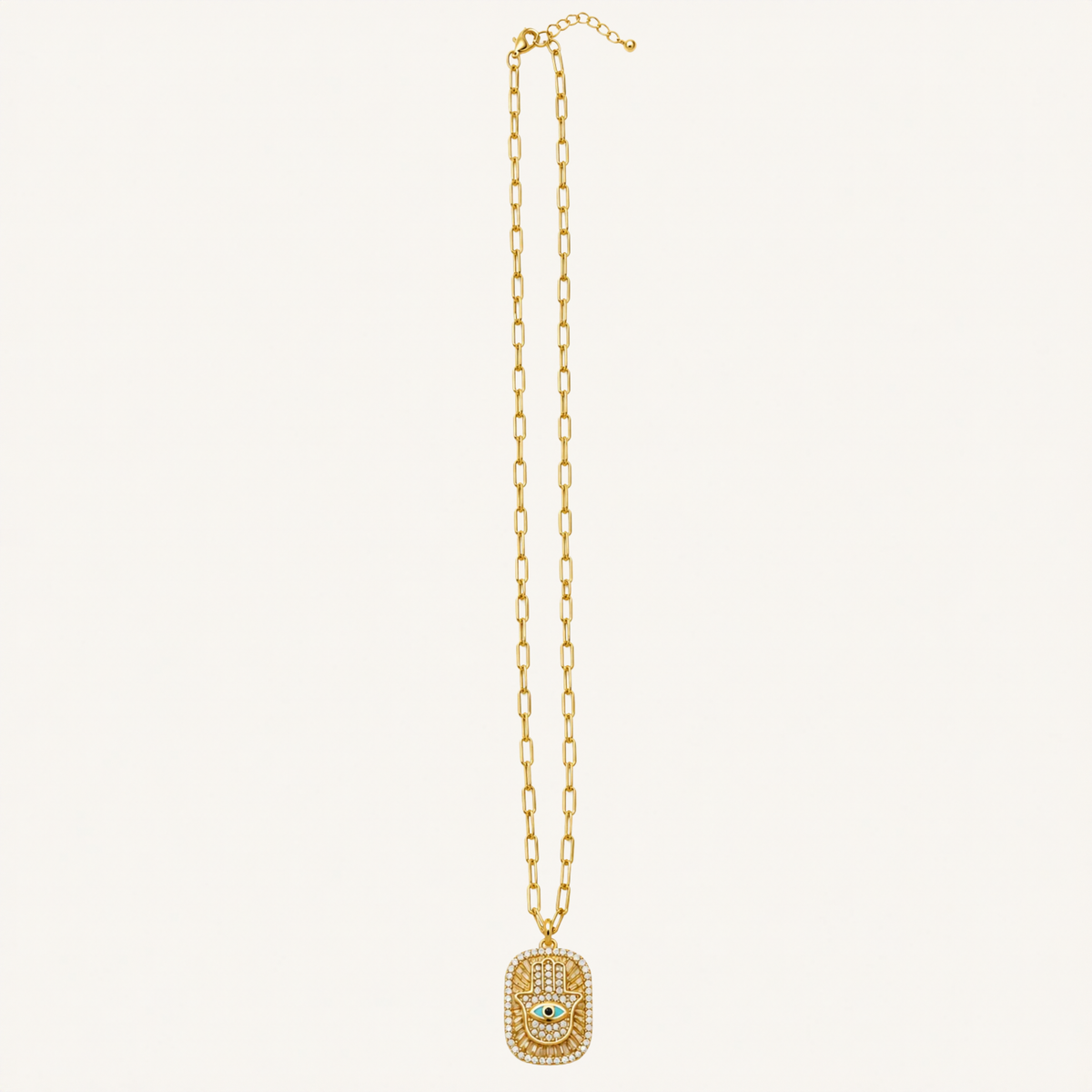 A gold chain necklace featuring a rectangular pendant encrusted with small clear stones and a central white stone, displayed against a solid off-white background.