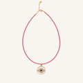 A pink beaded necklace with a gold-tone circular evil eye pendant, displayed on a clean off-white background.