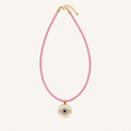 A pink and white twisted rope necklace with a gold-tone evil eye pendant, displayed on a clean off-white background.