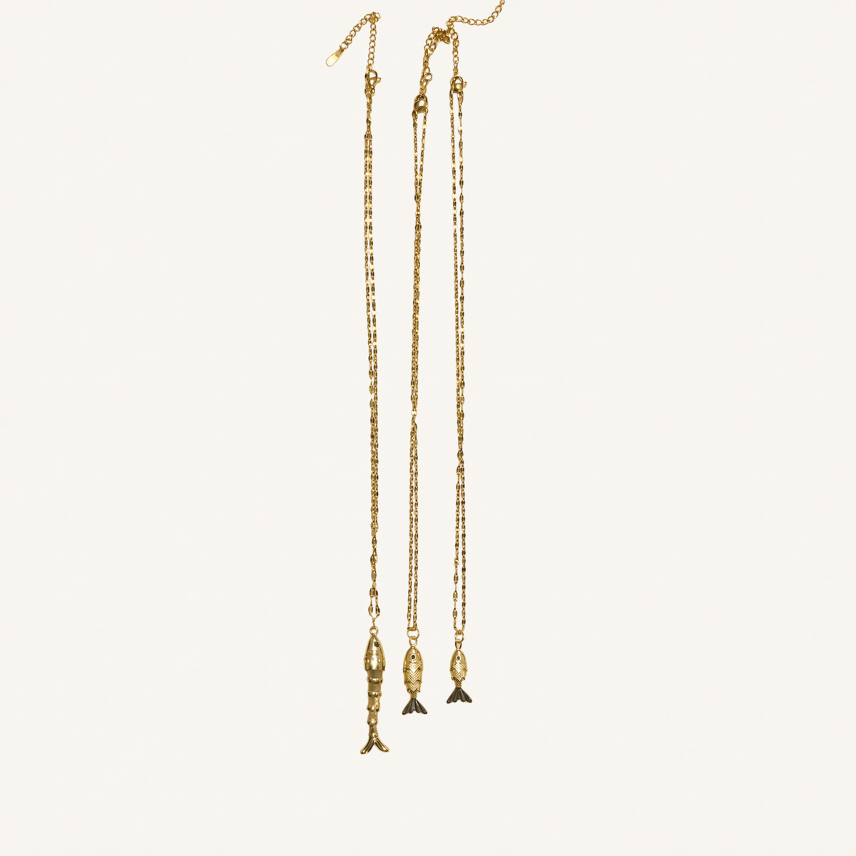 Three long gold-toned chain necklaces with dangling fish-shaped pendants, displayed against a plain off-white background.