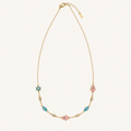A delicate gold chain necklace featuring a central pink hamsa hand charm, flanked by turquoise and pink hamsa charms, displayed on a light cream background.