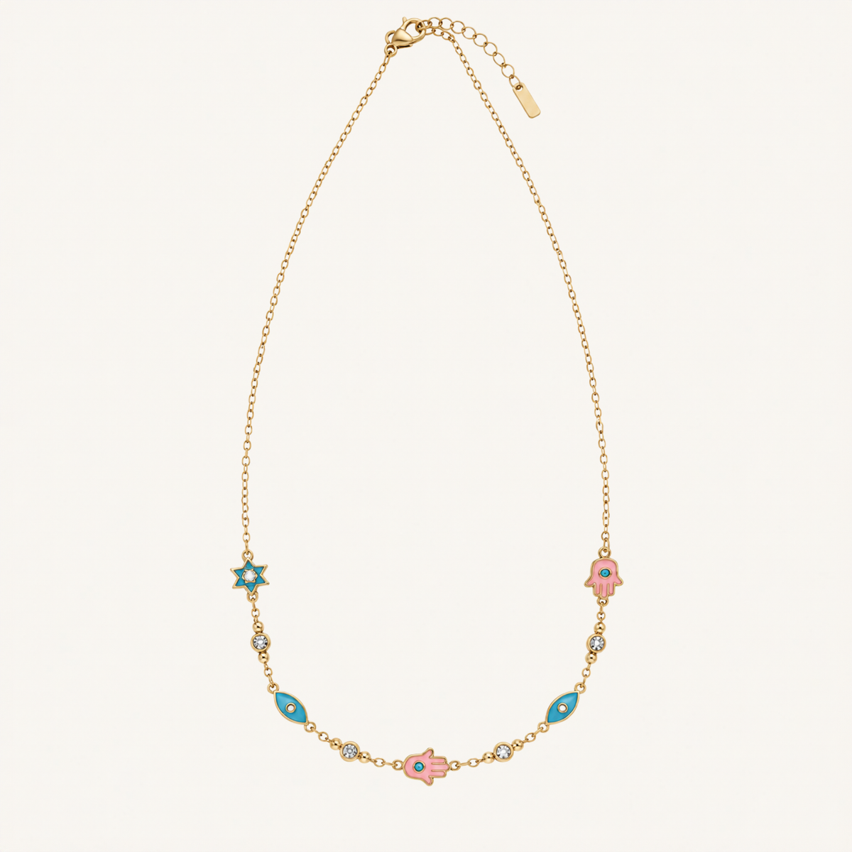 A delicate gold chain necklace featuring a central pink hamsa hand charm, flanked by turquoise and pink hamsa charms, displayed on a light cream background.