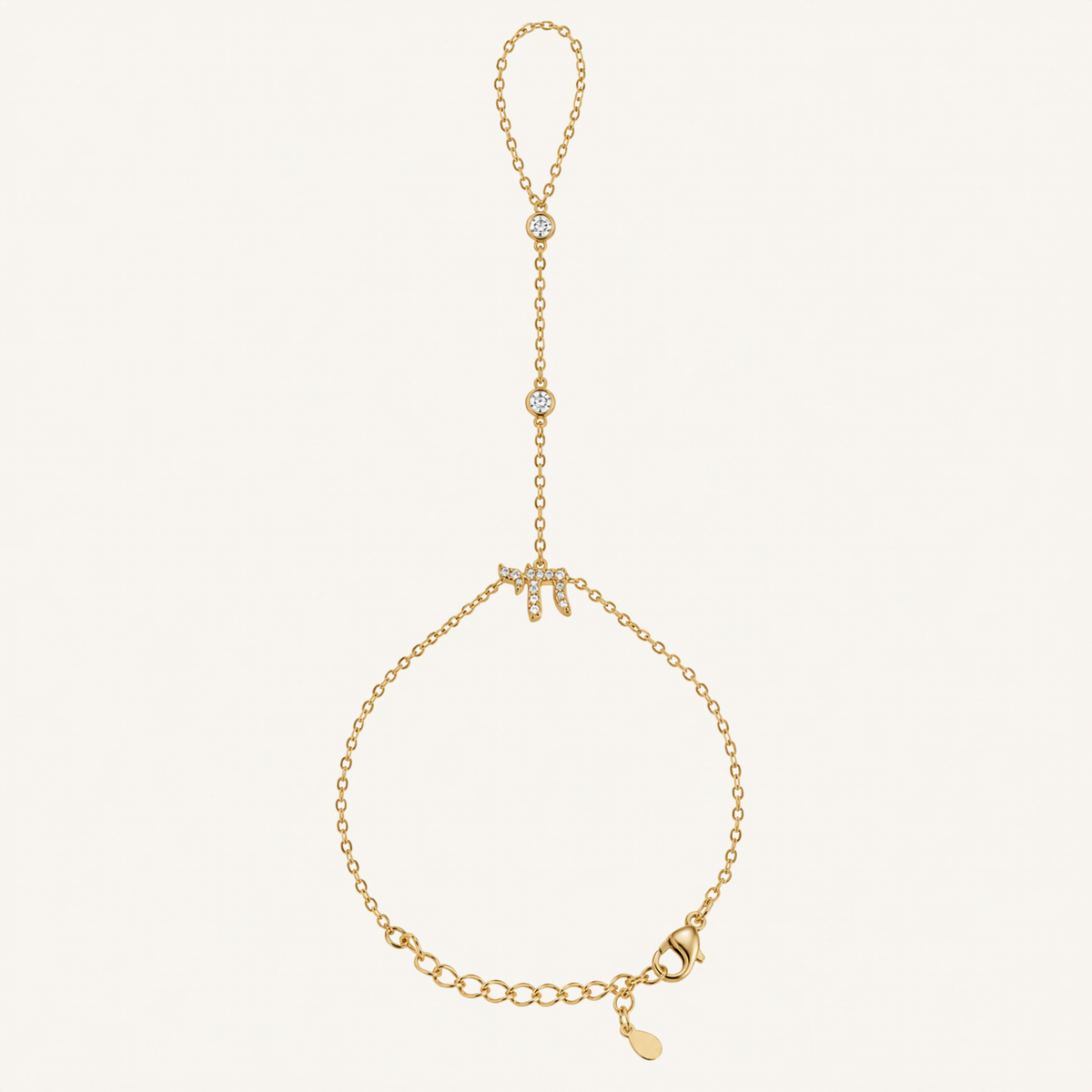 A delicate gold chain bracelet featuring a central letter 'M' embellished with small clear stones, a top loop with two small stone-set beads, and an adjustable chain closure with a small dangling tag, shown on a plain off-white background.